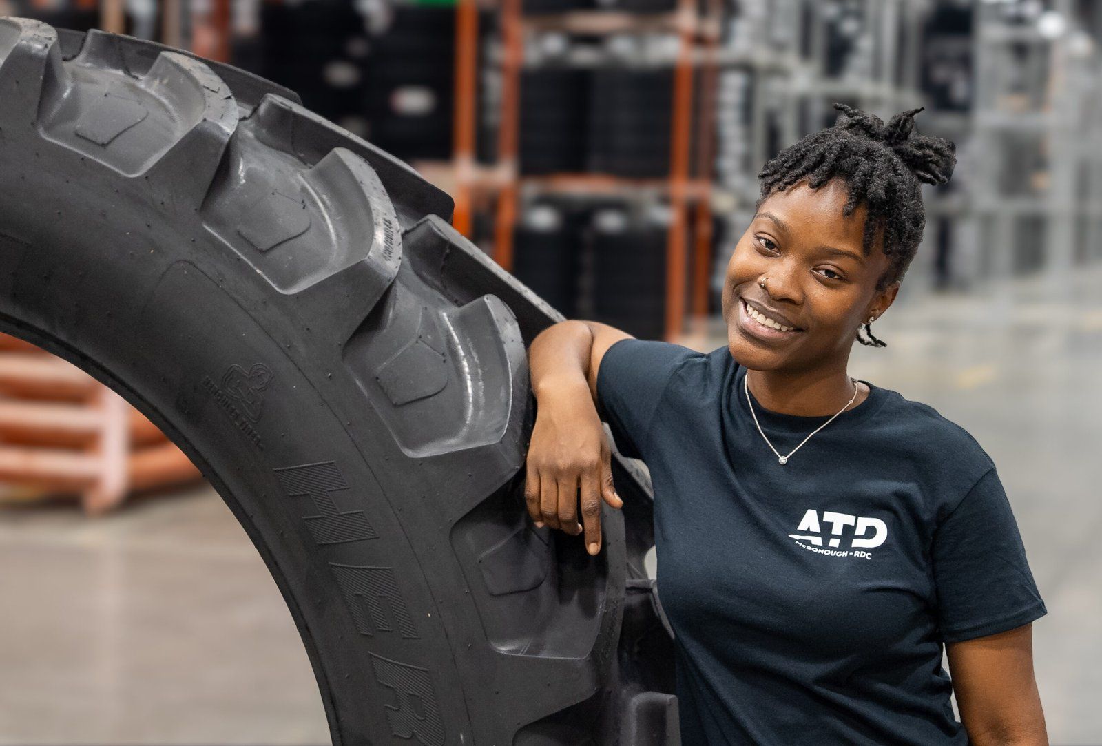 Warehouse associate leaning on an oversized tire, smiling